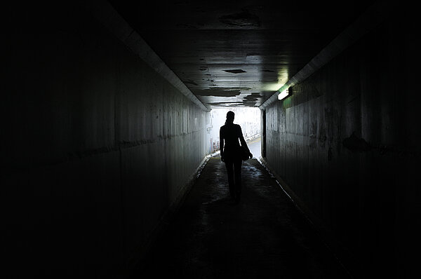 Schatten einer jungen Frau, die allein durch einen dunklen Tunnel läuft.