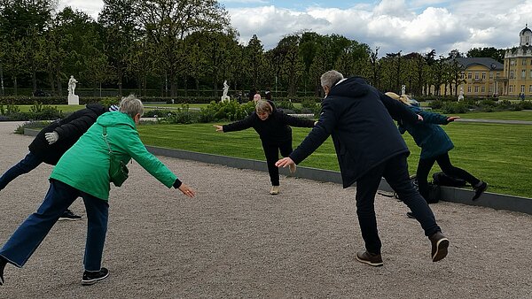 Personen vor dem Schloss Karlsruhe, die Gleichgewichtsübungen ausführen