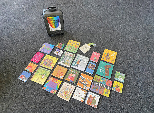 Eine Auswahl der Bücher liegen auf dem Boden und daneben steht der Regenbogenkinderbücherkoffer.