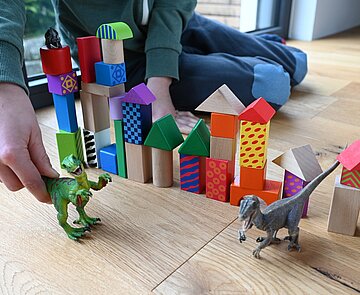 Bild spielt mit Dinosaurier und Bauklötzen.