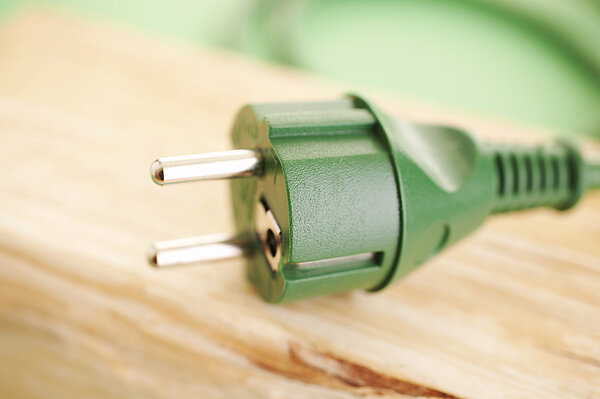 Das Bild zeigt einen grünen Stromstecker, der auf einem Holzbrett liegt.