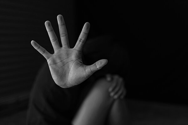 Person hockt auf Boden und hält Hand als Schutz vor Gesicht und Körper. 