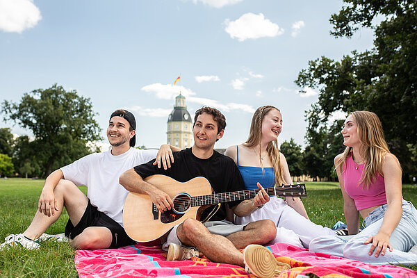 Studierendenstadt Karlsruhe  Werbefoto. Fröhliche junge Menschen auf Picknickdecke. Im Hintergrund das Karlsruher Schloss.