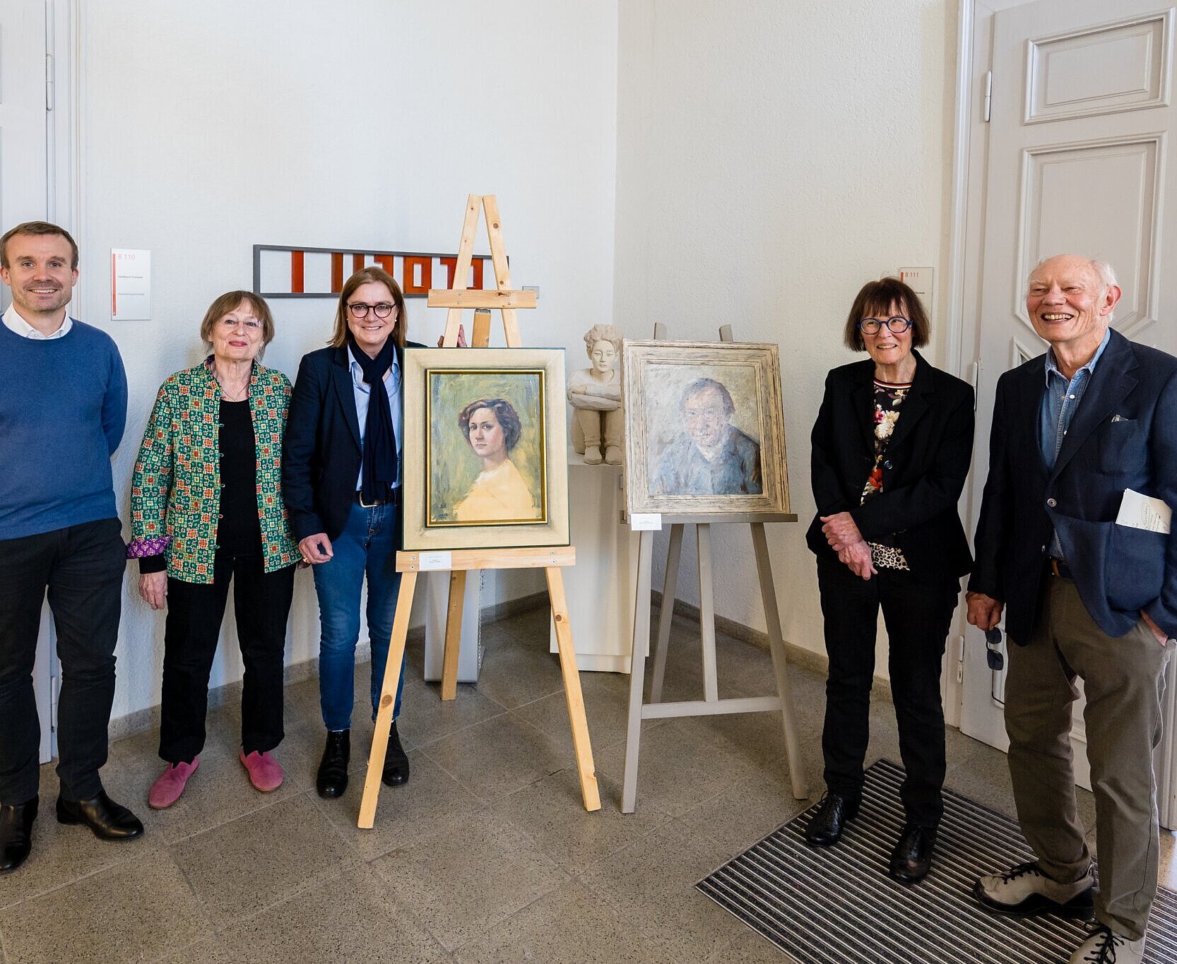 Ausstellung Schneider-Sato Die Portraits von Gerda Schneider (gemalt von Hardy Schneider-Sato, 1952) und Hardy Schneider-Sato (gemalt von Oskar Hagemann) – zur linken Seite: Ferdinand Leikam, Leiter der Historischen Museen der Stadt Karlsruhe, Kulturbeiratsmitglied Hildegund Brandenburg (Mitte) und Ortsvorsteherin Alexandra Ries; zur rechten Seite: Kulturbeiratsmitglied Erika Rödiger-Diruf und Wegbegleiter Eckhart Pilick.