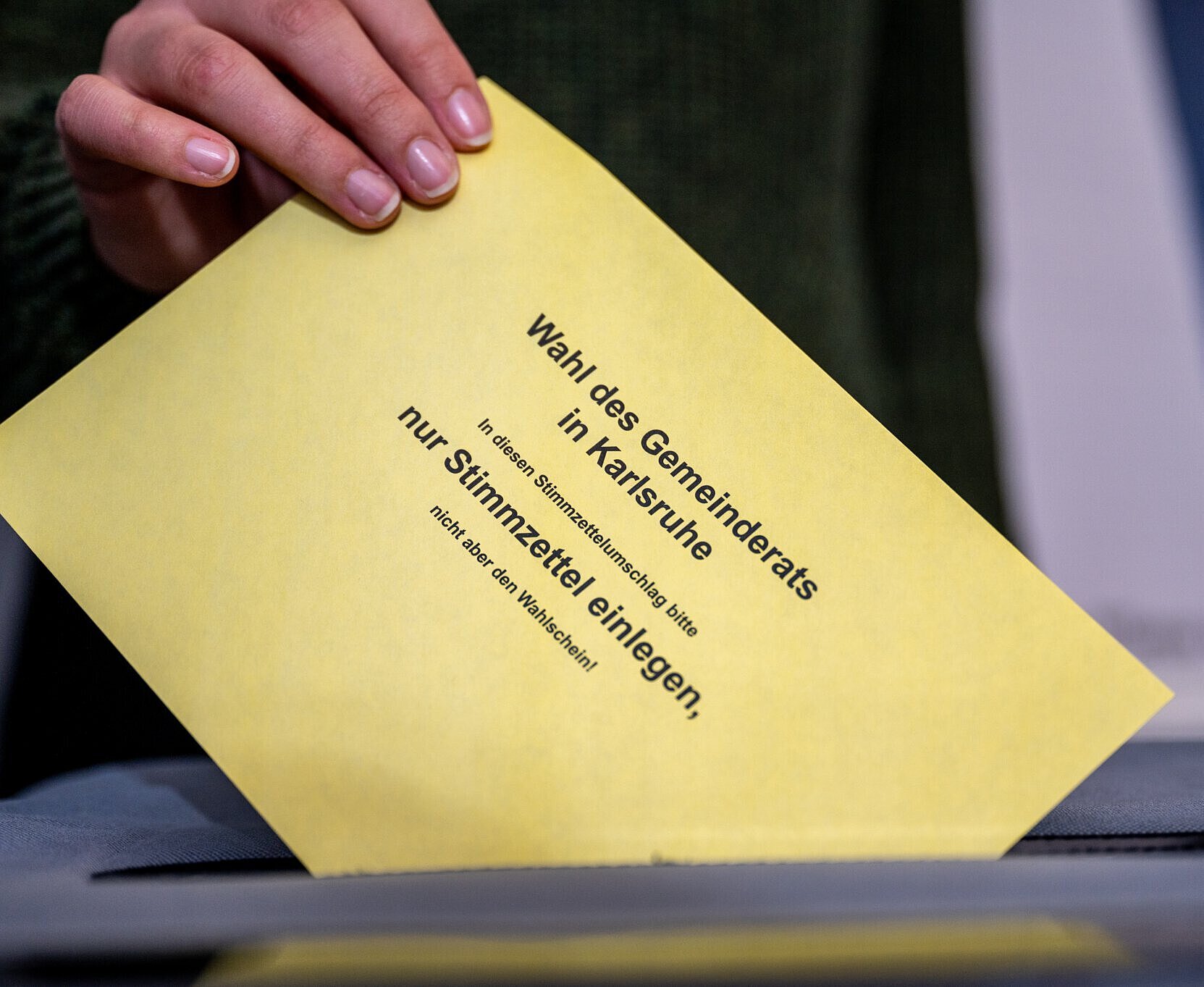 Wahlen 2024 Person wirft Stimmzettelumschlag für die Wahl des Gemeinderats in die Urne
