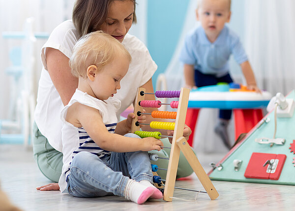 Kinder spielen auf dem Boden mit Lernspielzeug mit Erzieherin in der Kinderkrippe