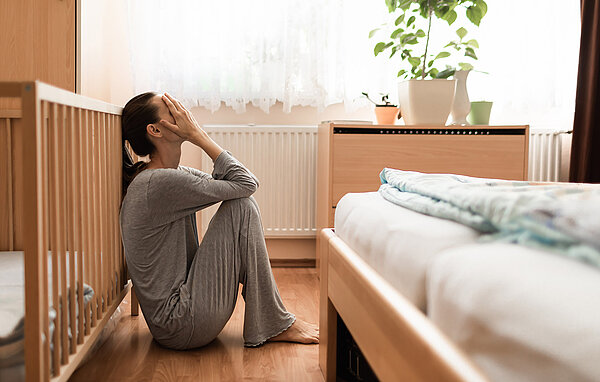 Frau sitzt verweifelt auf dem Boden zwischen Kinder- und Ehebett