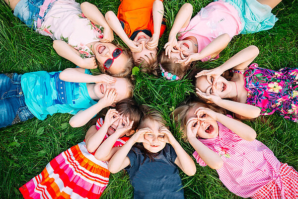 Kinder liegen im Kreis auf dem Rücken im Gras