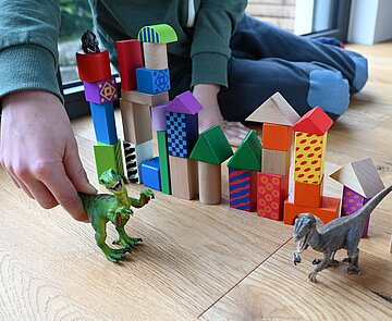Bild spielt mit Dinosaurier und Bauklötzen.