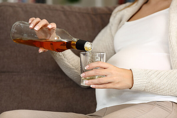 Unverantwortungsvolle, schwangere Frau gießt sich Alkohol ins Glas