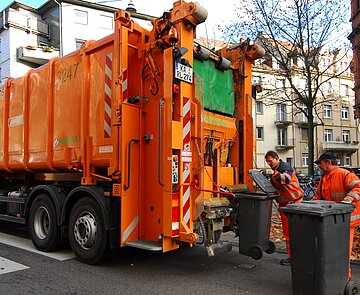 Müllabfuhr Müllwagen mit Abfalltonnen, die von zwei Mitarbeitern geleert werden
