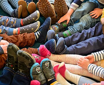 Kindergarten Kinder sitzen im Kreis auf dem Boden und strecken ihre Beine in die Mitte.