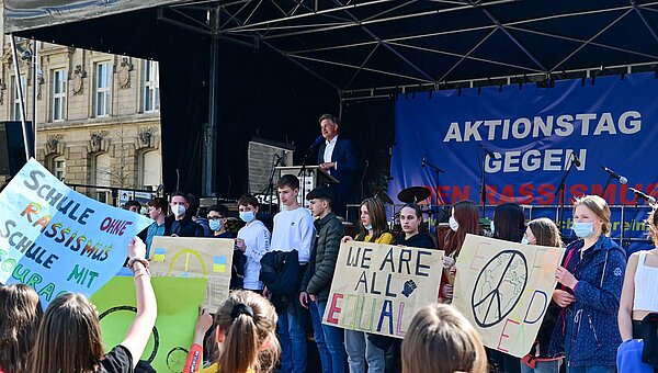 Aktionstag gegen Rassismus 2022 Schülerinnen und Schüler stehen beim Aktionstag gegen Rassismus mit Plakaten vor einer Bühne, auf der Oberbürgermeister Dr. Frank Mentrup spricht.