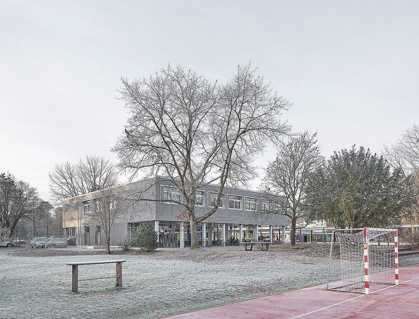 Das Bild zeigt die Nordwestperspektive des Gebäudes D, die teilweise von Bäumen verdeckt ist und den Schulhof.