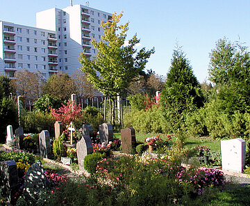 Das Bild zeigt den Friedhof Oberreut mit einigen Gräbern und Hochhäusern im Hintergrund. 