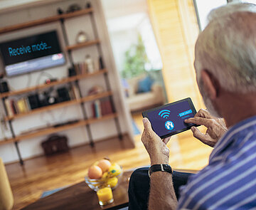 Älterer Herr mit Fernbedienung in der Hand.