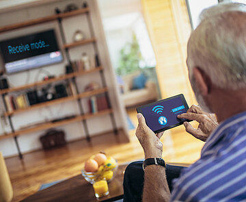 Älterer Herr mit Fernbedienung in der Hand.