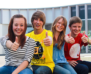 Vier Jugendliche, die in die Kamera lachen und Daumen nach oben zeigen.