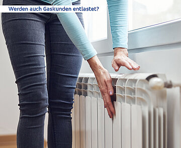 Man sieht den Unterkörper einer Frau. Mit den Händen berührt sie einen Heizkörper