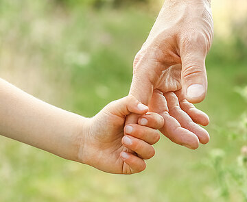 Nahaufnahme einer Kinderhand, die sich an einer Erwachsenenhand festhält.