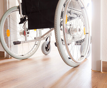 Das Bild zeigt einen rollstuhlfahrenden Mensch, der durch Türrahmen fährt.