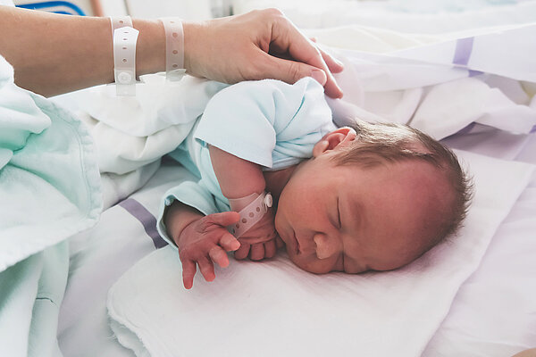 Ein neugebores Baby liegt im Krankenhausbett