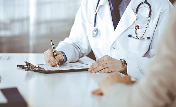 Arzt und Patientin, die etwas besprechen, während sie in der Klinik sitzen und ein Klemmbrett benutzen