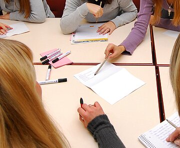 Person zeigt am Tisch mit Schreibgerät auf ein Schriftstück.