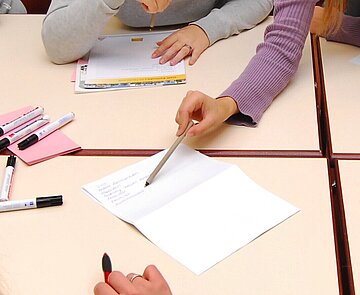 Person zeigt am Tisch mit Schreibgerät auf ein Schriftstück.