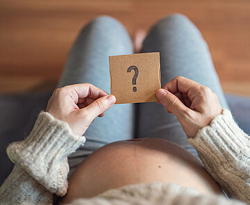 Schwangere Frau hält Papier mit Fragezeichen