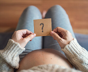 Schwangere Frau hält Papier mit Fragezeichen
