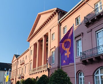 Auf dem Bild ist das Karlsruher Rathaus zu sehen, vor dem die Fahne zum Internationalen Frauentag am 8. März weht. 
