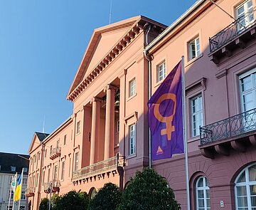 Auf dem Bild ist das Karlsruher Rathaus zu sehen, vor dem die Fahne zum Internationalen Frauentag am 8. März weht. 