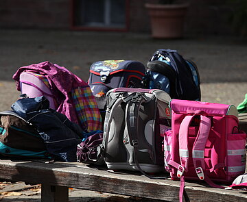 Mehrere Schulranzen stehen auf einer Bank