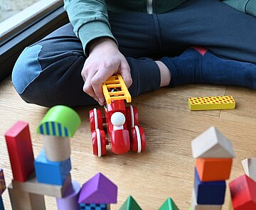 Eine Kinderhand schiebt eine Spielzeugfeuerwehr vor Bauklötzen.