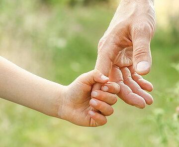 Nahaufnahme einer Kinderhand, die sich an einer Erwachsenenhand festhält.