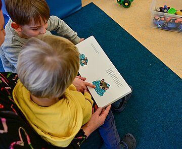 Eine Erzieherin liest mit zwei Kindern ein Buch.