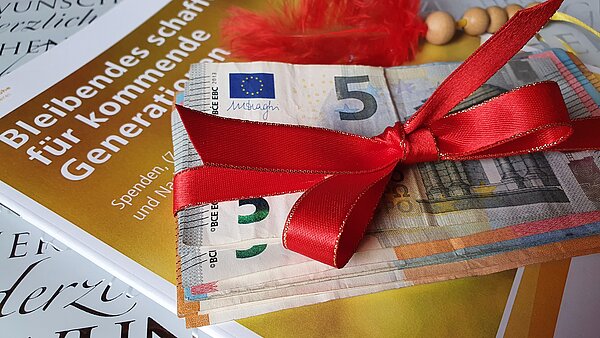 Geldscheine als Geschenk verpackt auf der Broschüre "Bleibendes schaffen"