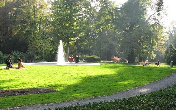 Das Bild zeigt einen Teil des Schlossgarten Durlach mit Spielplatz, einem Brunnen und einer Liegewiese. 