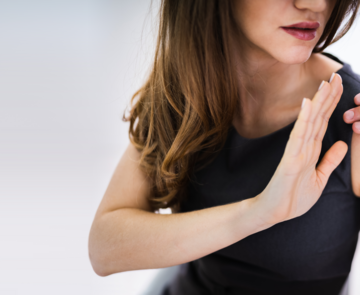 Frau wehrt mit ihrer Hand die Hand eines Mannes ab, der ihr auf die Schulter fasst. 