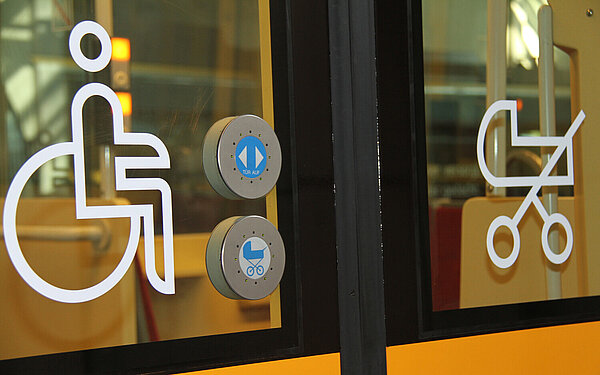 Die Abbildung zeigt eine Straßenbahntür mit Symbolbildern für Rollstuhlfahrende und Familien