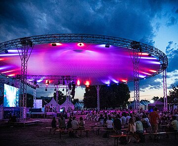 Zu sehen ist das magisch beleuchtete Dach der EFFEKTE-Bühne mitsamt Publikum bei Nacht