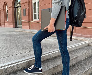 Junger Mann mit Ordner und Rücksack der die Treppe zum Rathaus hochsteigt.