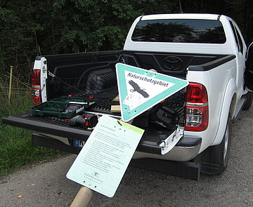 Das Bild zeigt ein weißes Dienstfahrzeug der Feldhut, mit dem eine Schutzgebietstafel transportiert wird.