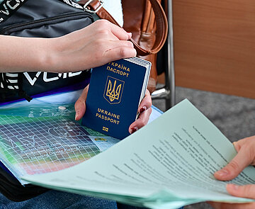 Das Bild steht symbolisch für die Ukrainehilfe. Es Zeigt Hände, die einen Pass und Formulare halten.