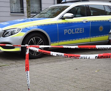 Das Bild zeigt ein Polizeiauto vor einer Absperrung.