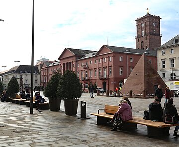 Marktplatz mit besetzten Bänken, im Hintergrund Pyramide und Rathaus