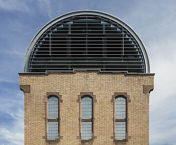 Nahaufnahme der westlichen Giebelseite des Tonnendachs mit Fensterband, die restlichen Teilflächen sind aus geschlossenen Paneelen.