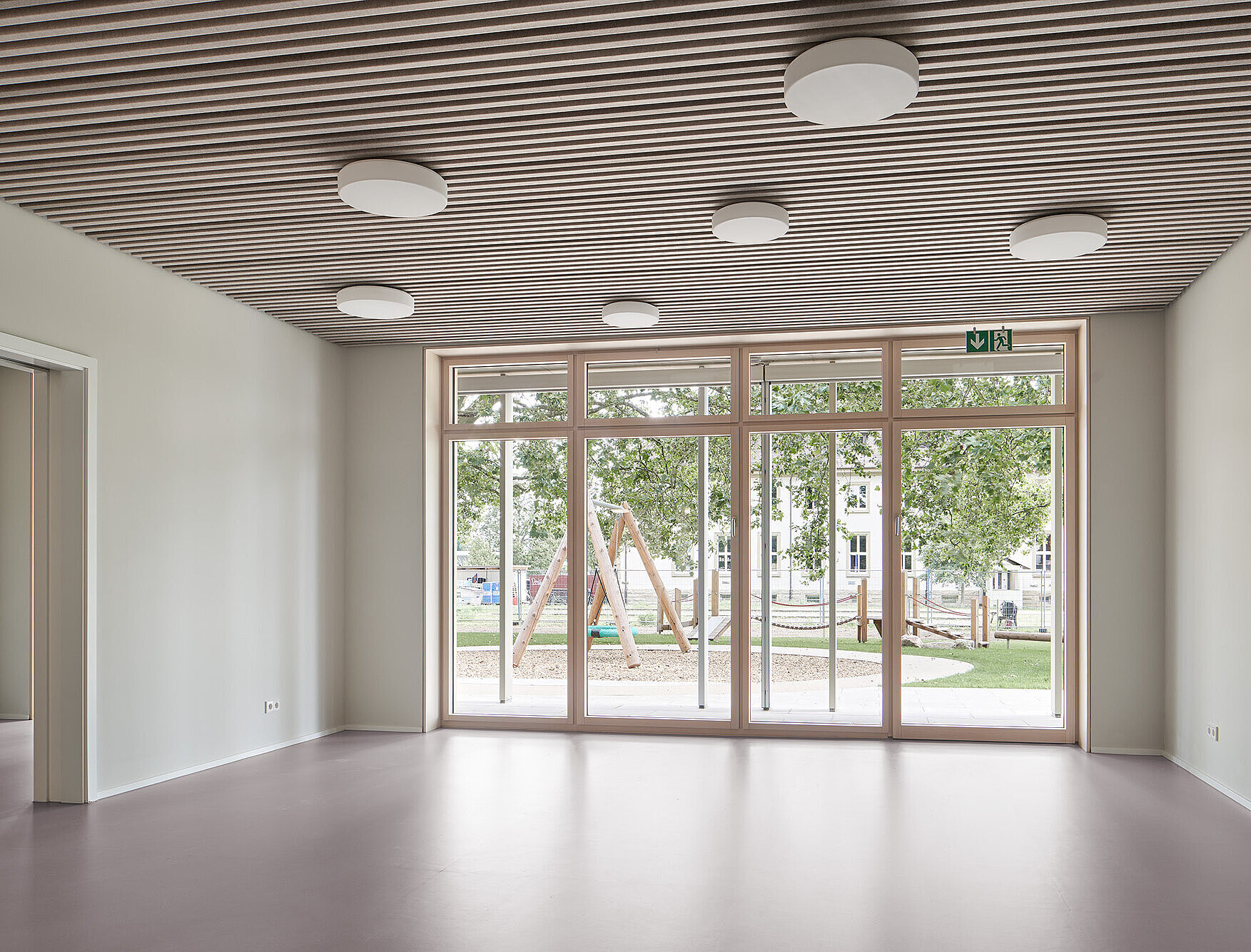 Das Foto zeigt die großen Holzfenster, durch die man in den Spielgarten blicken kann.