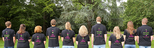 Menschen stehen in einer Reihe, der T-Shirt Rücken ist beschriftet